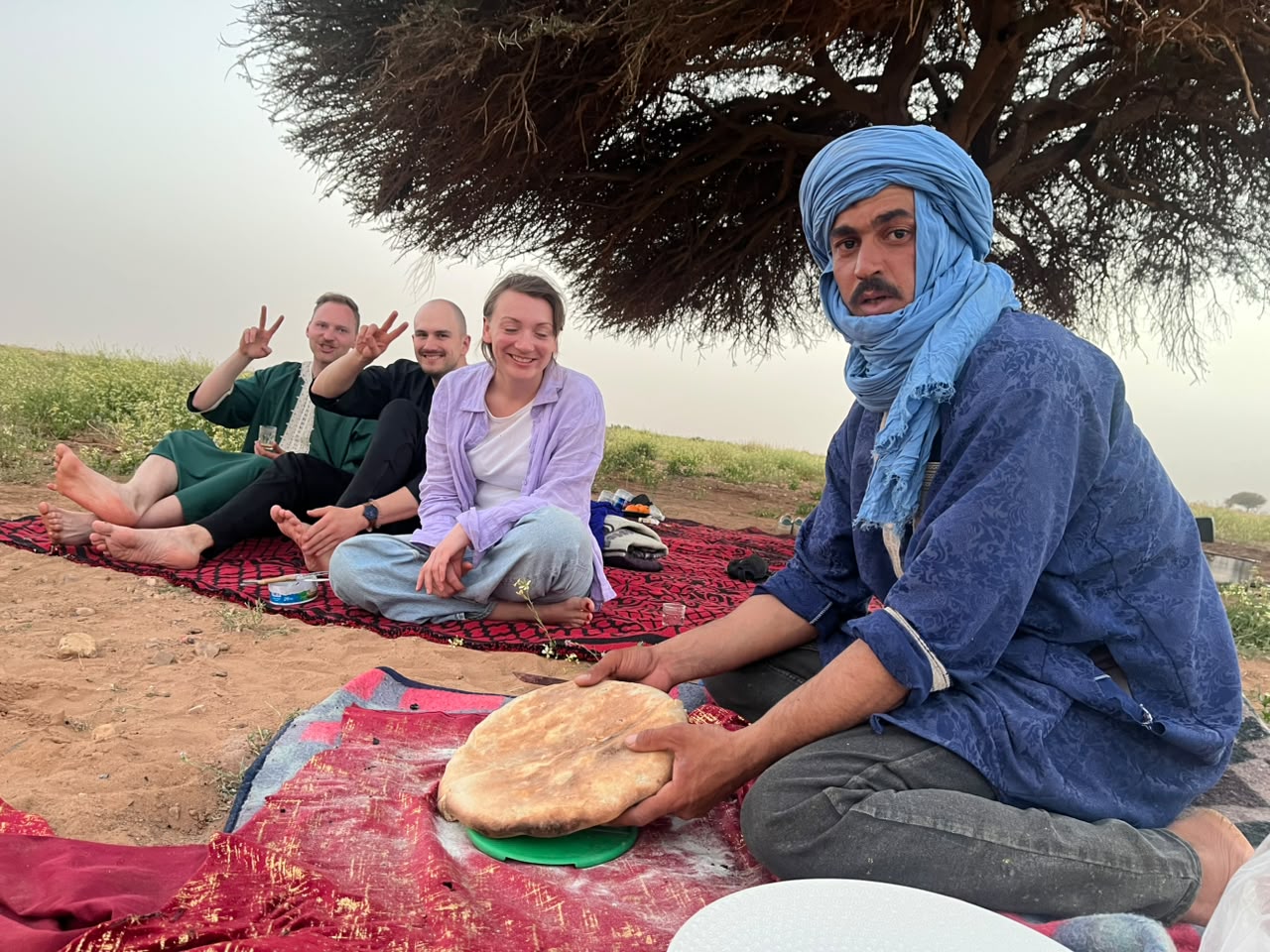 Bread and tea shared on rugs under an acacia tree
