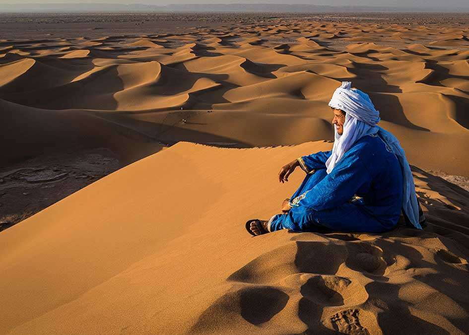 A man in blue watching the dunes from a crest